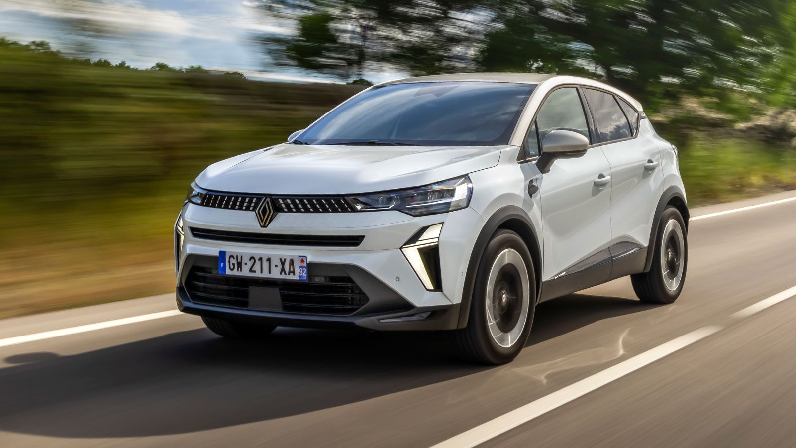 Εμπρός λήψη από το Renault Captur να κινείται σε δρόμο με δέντρα στο φόντο.