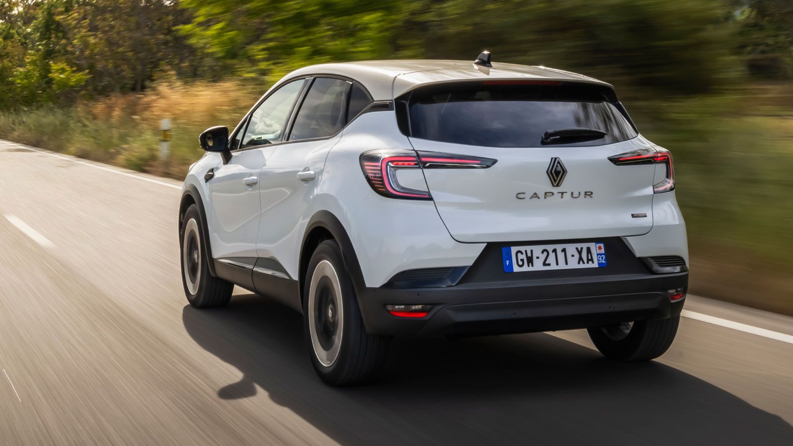 Πίσω όψη από το Renault Captur να κινείται σε δρόμο με δέντρα στο φόντο.